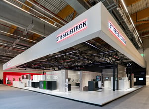 Messestand von STIEBEL ELTRON auf der ISH 2025 mit modernem Design, grauen und roten Akzenten sowie Präsentationsflächen für Heiz- und Energielösungen.