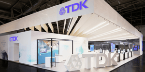 Perspective of TDK’s modern booth with striking lighting and visitors engaging with the exhibits.