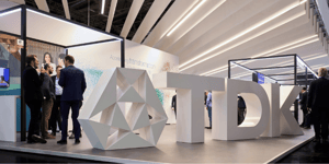 Side view of TDK’s booth at electronica 2024 with visitors and a large geometric structure next to the TDK logo.