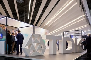 Seitenansicht des TDK Messestandes auf der electronica 2022 mit Besuchern und einer großen geometrischen Struktur neben dem TDK-Logo.