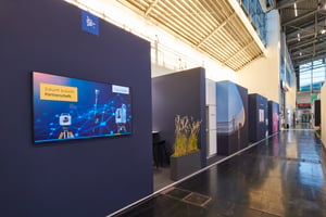 Side view of the Trimble exhibition stand featuring an LED screen, dark architectural elements, integrated plants and an open walkway.