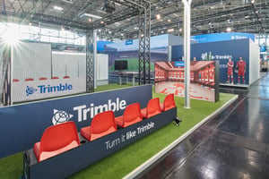 Trimble exhibition stand featuring an interactive football-themed area, stadium seating and large digital displays inside an exhibition hall.