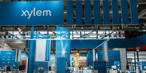 Front view of the Xylem exhibition stand with a blue-green suspended ceiling, LED displays, seating areas and suspended graphic elements.