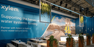 View of the Xylem exhibition stand, showing the seating and dining area with a large printed exhibition wall in the background.