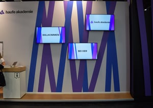 Wall of the Haufe Group booth with multiple screens and a striking purple pattern for brand presentation.