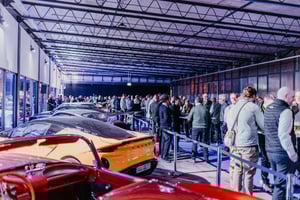 Besucher bewegen sich durch einen ZEISS‑Roadshow‑Ausstellungsbereich mit Sportwagen und beleuchteten Produktpräsentationen.