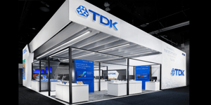 Full view of the TDK booth at CES 2025 with an open design, white walls, and large TDK logos. Blue screens and exhibits in the foreground.