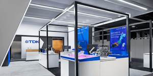 Interior view of the TDK booth at CES 2025 featuring a clean structure with black frames and white tables. Blue screens highlight topics such as ‘Information & Communications Technology.’