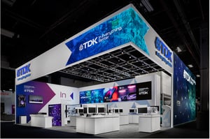 Eckansicht des zweistöckigen TDK Messestands auf der CES 2026 mit großformatigen LED‑Visuals und offener Architektur.