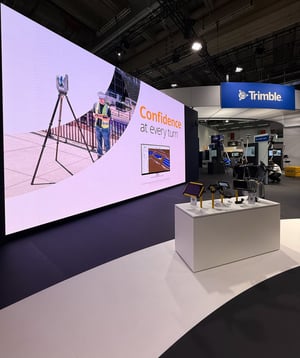 Trimble booth at Intergeo 2025 in Frankfurt featuring a large LED display, surveying technology presentations, and a central information desk.
