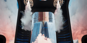 Innenraum mit großem Bildschirm, der Raketenantriebe mit Rauch oder Dampf zeigt; einige Personen stehen davor.