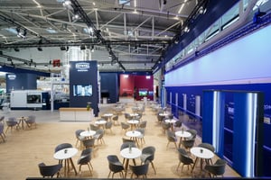 Gesamtansicht des Krones Messestandes mit zahlreichen Sitzplätzen, blauer Markenwand und Präsentationsflächen für Getränke- und Verpackungslösungen.